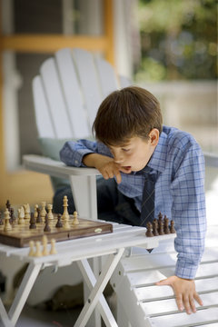 Boy sitting on deckchair and playing chess outdoors