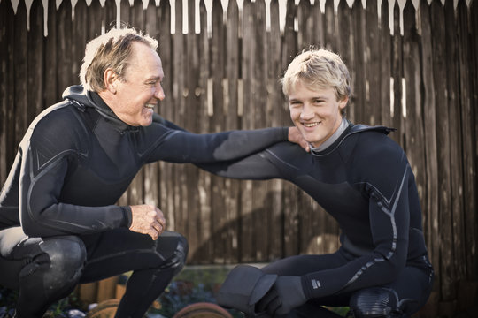 Portrait of a smiling young man wearing a wetsuit and with his arm around his father.