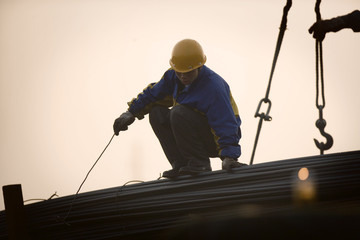 Young adult male construction worker atop steel poles attached to a crane on a wharf.