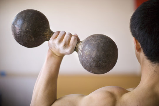 Young adult boy lifting dumbbells in a gym.