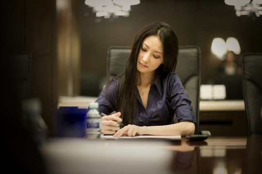 Young adult business woman taking notes in a boardroom.