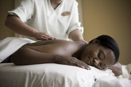 Content mid adult woman lying on a massage table with her eyes closed while being massaged by a therapist.