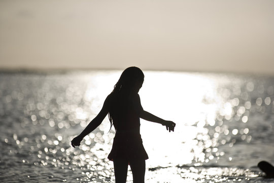 Silhouette of a girl standing in the shallows on a beach at sunset.