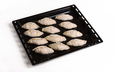 Pies ready for baking lying on a black steel baking sheet. Three quarters view from above