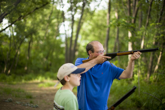 Man and young boy aiming rifles in forest