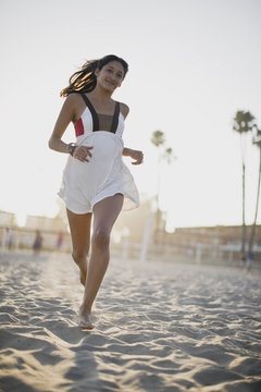 Portrait of a teenage girl running along a beach at sunset.