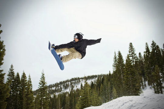 Young man jumping mid-air while riding his snowboard  outdoors in the snow.