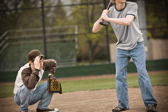 Teenage boy crouching with a baseball mitt behind a batsman on a sports field.