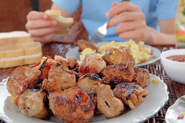 Pieces of fried meat in the white plate on the wicker table on the open air. The national dish of middle East. Closeup view, selective focus.