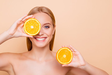 Pretty charming joyful attractive cheerful funny comic positive nude natural pure girl having two pieces of orange, closing one eye, isolated on beige background with copy space for advertisement