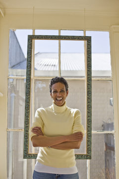 Portrait of a laughing mid-adult woman standing in front of a window with her arms crossed.