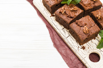 Brownie sweet chocolate dessert with walnuts and meant leaves on retro board with copy space on pastel beige background.