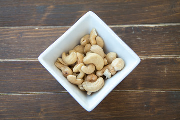 cashew nuts inside white bowl on a wooden table viewed from above