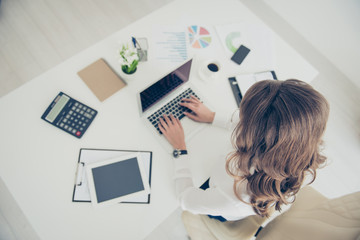 Top view portrait of woman with curls, hairdo holding hands on keyboard making presentation, project, report, having accessories on her desk sitting on armchair using wi-fi internet