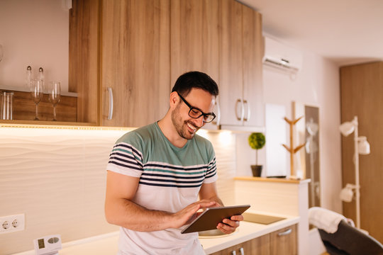 Handsome young man working on a tablet computer while standing in his modern kitchen - Powered by Adobe