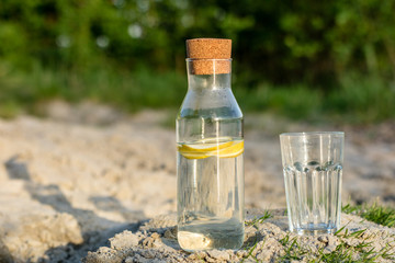 Obraz na płótnie Canvas A bottle of water with lemon and a glass. Drink set in the grass by the lake