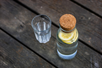 A bottle of water with lemon and a glass. A bench on which a refreshing drink is placed.