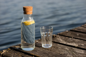 A bottle of water with lemon and a glass. Bridge on which stands a refreshing drink.