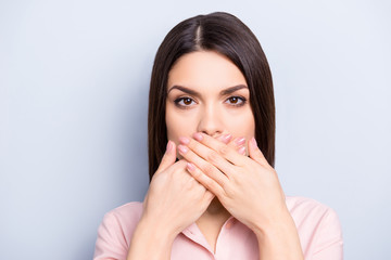 I can't speak! Portrait of pretty charming brunette woman closing her mouth with two crossed palms isolated on grey background, looking at camera