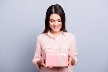 Obraz premium Portrait of glad, charming pretty, trendy woman having gift box in pink package with white bow looking at present isolated on grey background