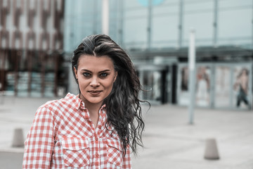 A toned-up portrait of a smiling and satisfied woman. A young and attractive girl looks ahead against the background of the shopping center. Retro style.