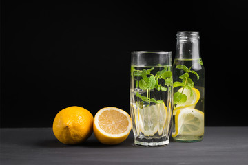 The concept of holidays and parties, food and drinks. Cold alcoholic cocktail mojito, lemonade with lemon, mint and ice in a glass and a bottle on a black background. Copy background space