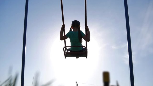 Happy little girl have fun sway spin on a swing on nature sunset. A silhouette young girl swings on a swing.