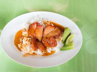 Red pork with rice, topped with red water in the dish, white on green table.