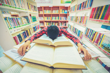 Tired male university student sleeping on books at desk in library