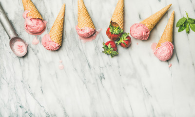 Healthy low calorie summer dessert. Flat-lay of homemade yogurt ice cream with strawberries in waffle cones over grey marble background, top view, copy space. Clean eating, dieting food concept
