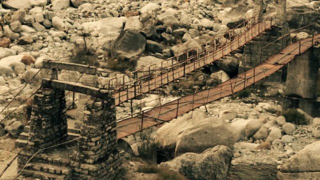 Suspension bridge over river, pendant bridge, monkey bridge. Winter period, the bottom of the river bare, huge boulders. Valley of river Parvati, During monsoon rains it is mad river. Himalayas
