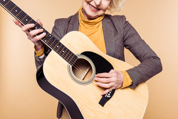 cropped image of stylish woman playing on acoustic guitar isolated on beige background