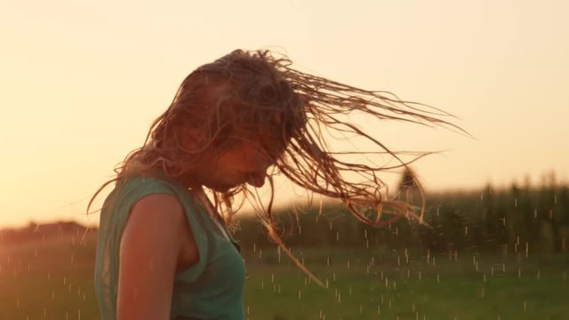SLOW MOTION, CLOSE UP, LENS FLARE: Attractive young Caucasian woman playfully flips her long wet hair left and right while she dances completely relaxed on a picturesque golden lit spring morning.