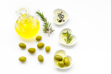 Fresh olive oil in glass jar near green olives and branch of rosemary on white background top view copy space