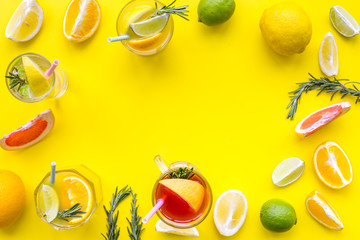 Concept of alcoholic cocktail with fruits. Glass with beverage near oranges, grapefruit, lime and rosemary on yellow background top view copy space