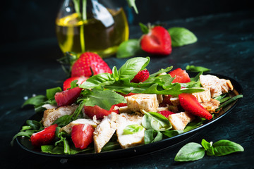 Salad with arugula, strawberries and chicken, dark background, selective focus