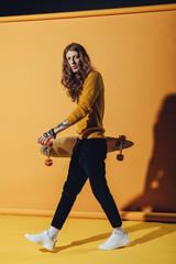 Fototapeta na wymiar stylish tattooed skateboarder with longboard, on yellow
