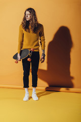 Fototapeta na wymiar elegant stylish man posing with skateboard, on yellow