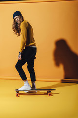 Fototapeta na wymiar handsome stylish man standing on skateboard, on yellow