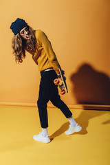 Fototapeta na wymiar stylish young skater posing with longboard, on yellow