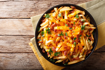 Freshly cooked French fries baked with cheddar cheese, bacon and parsley closeup. horizontal top...