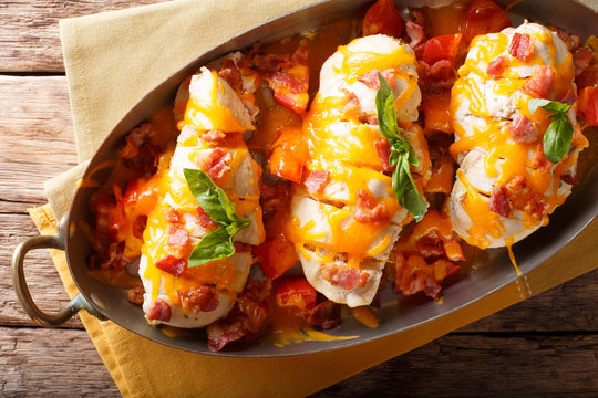 Spicy chicken fillet baked with bacon, tomatoes and cheddar cheese close-up in a pan. horizontal top view