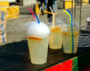 Cold soft drinks lemonade in plastic cups with , straws on display at a street market.