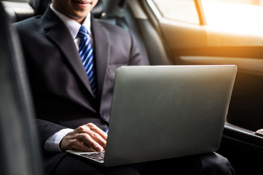 Handsome Young Businessman Using Laptop And Sitting In Back Seat Of Car.