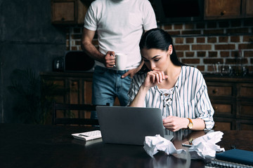 stressed young woman counting bills while her husband standing behind