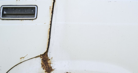 Rust and dents on the body of a white car