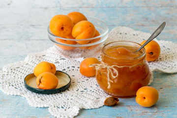 Sweet dessert. A small round jar with homemade jam and fresh ripe apricots on an openwork knitted napkin on an old wooden table. 