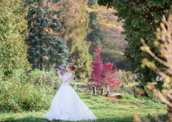Beautiful bride walks with violet wedding bouquet around green backyard