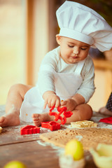 The small baby sits on the table near dough