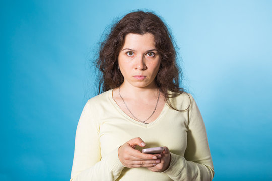Portrait angry young woman holding mobile phone isolated over blue background